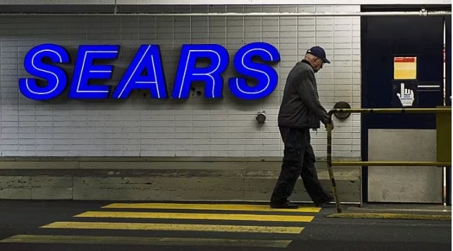 Man with a cane walking by a sears sign