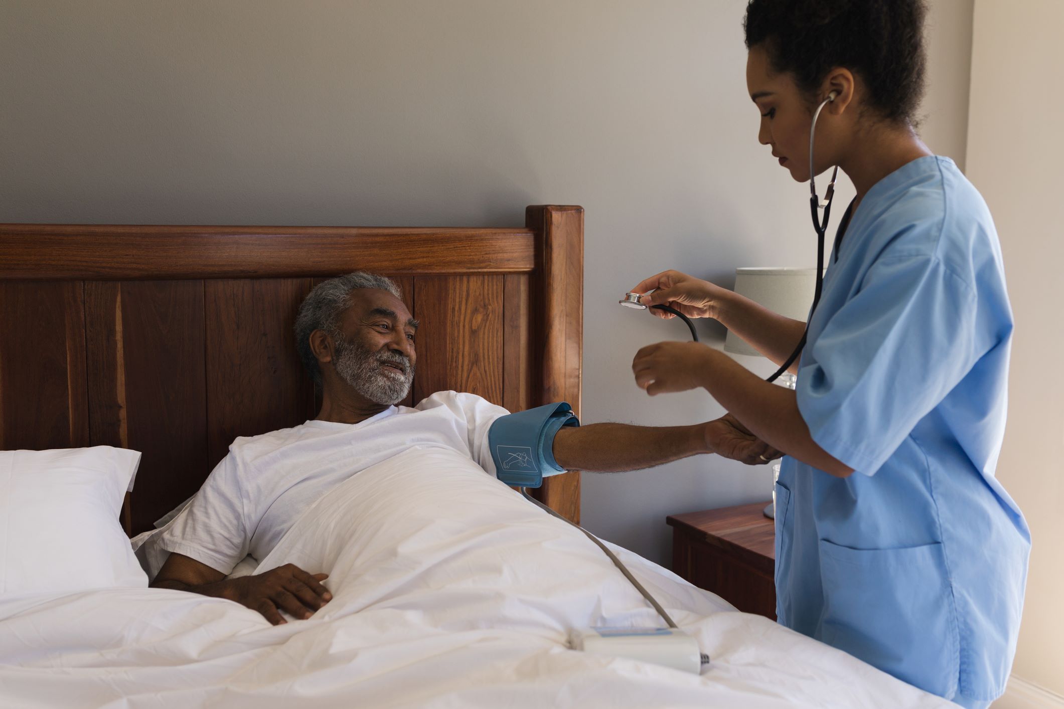 Elderly man getting blood pressure taken by a health care worker in his bed at home.