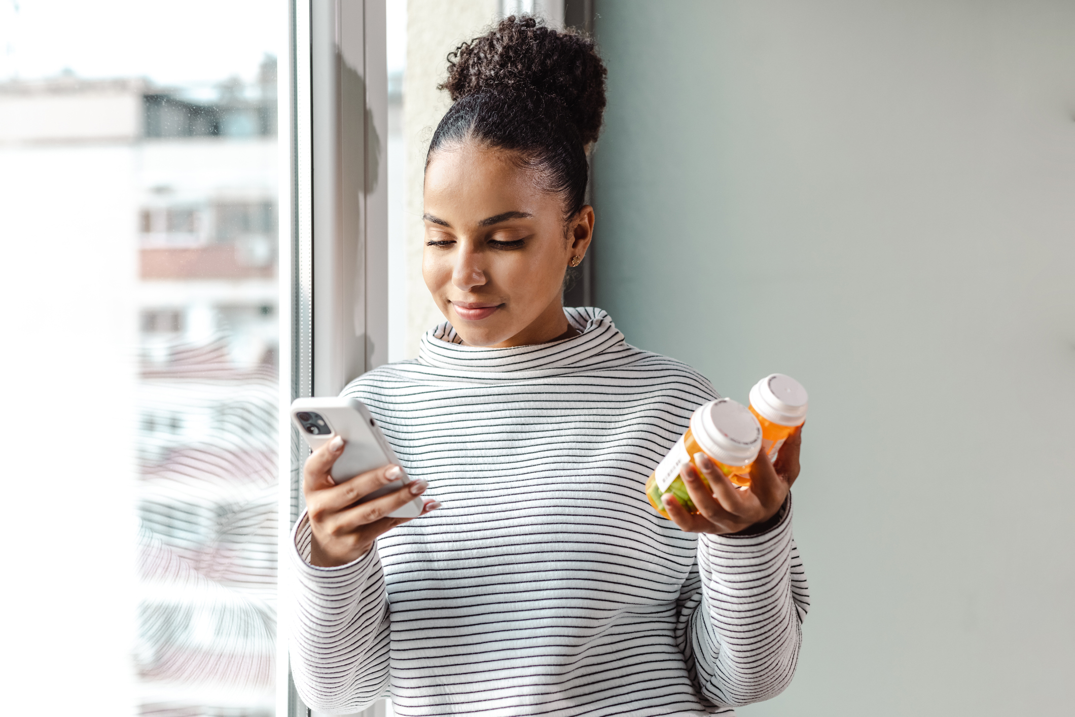 young woman holding 2 prescription bottles and looking on her phone