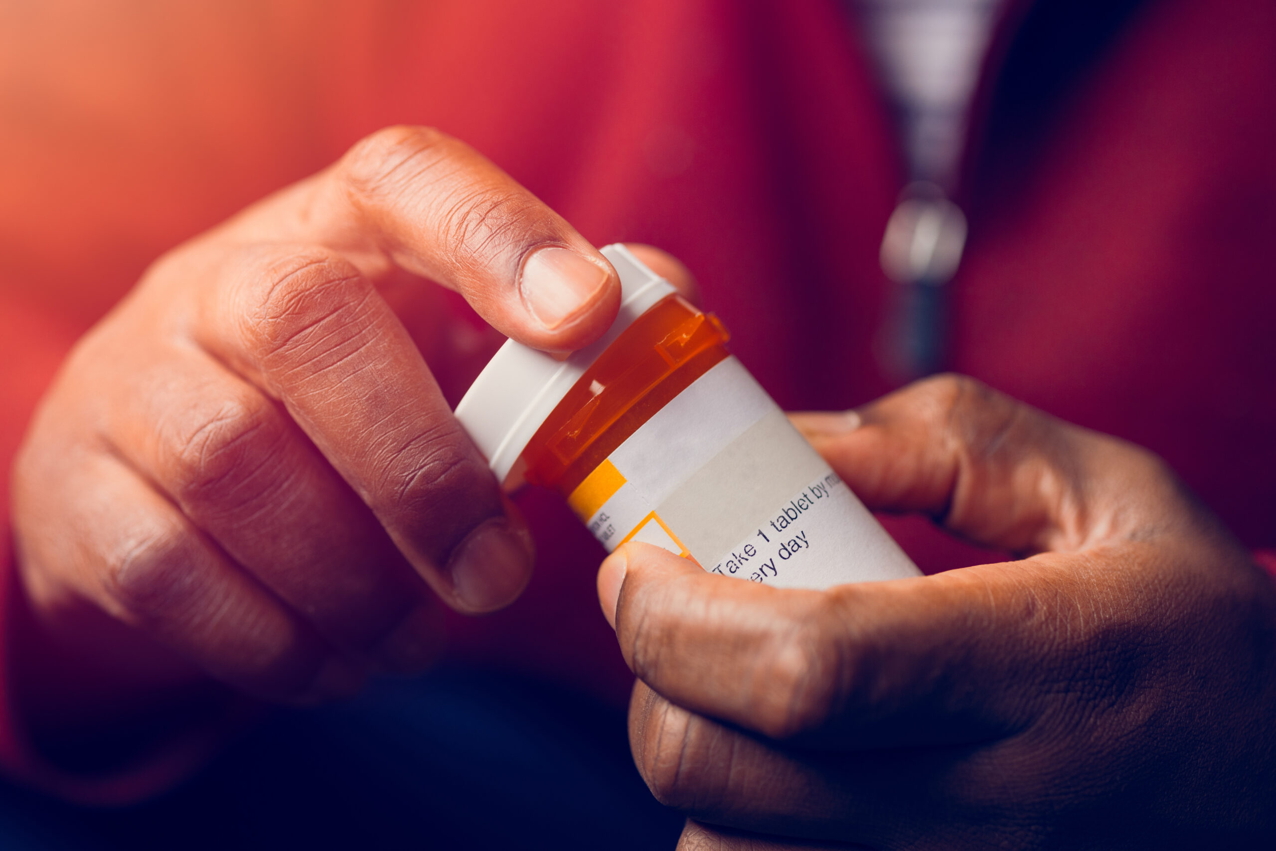 close up of man sitting down handling prescription pill bottle about to pour pills out